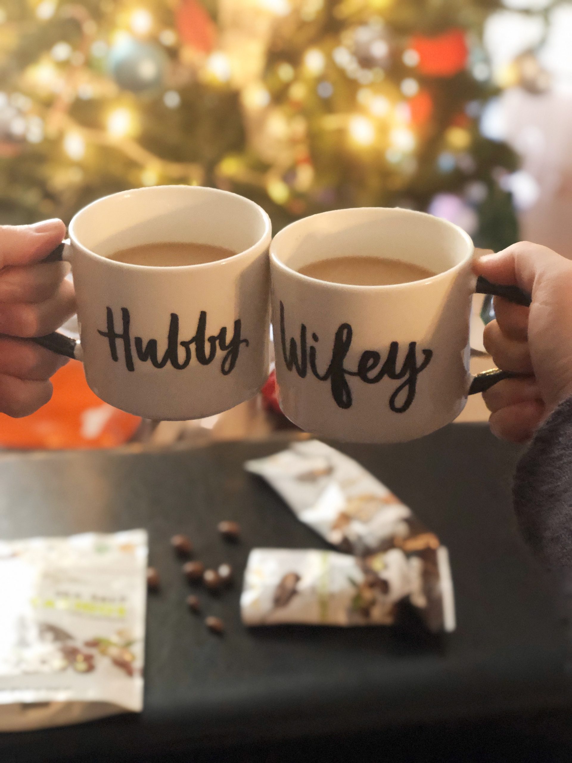 Hubby and Wifey coffee cups in front of a Christmas tree with chocolates.