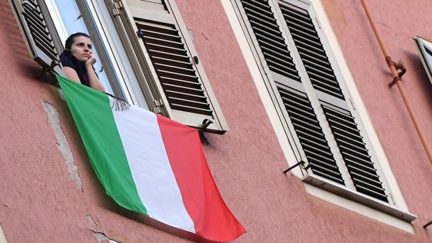 Mulher na janela, abaixo da qual se vê bandeira da Itália
