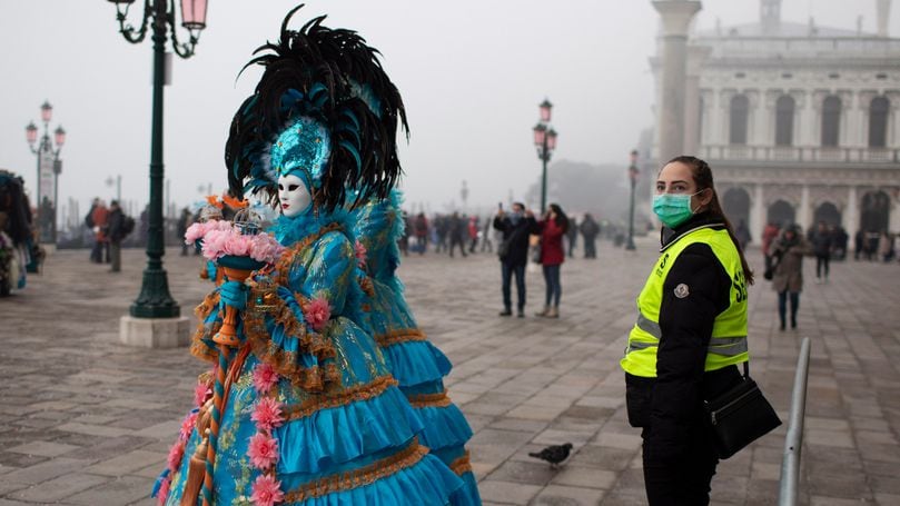Venice (Italy), 23/02/2020.- A security guard wearing a protective face mask stand guard as masked and costumed people walk by on the streets of Venice near San Marco square during the Carnival in Venice, Italy, 23 February 2020. (Italia, Niza, Venecia) EFE/EPA/ABIR SULTAN
