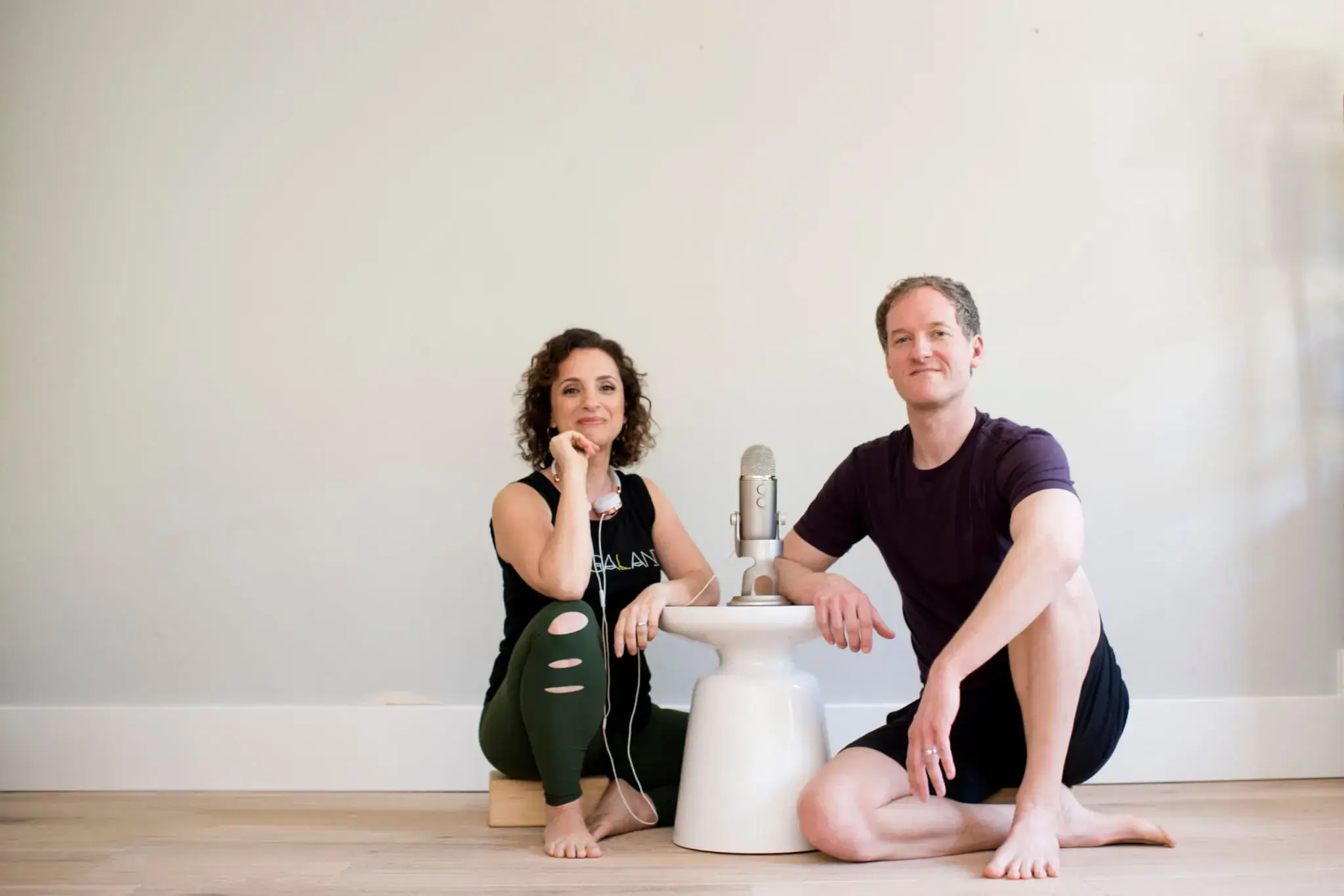 Andrea Ferretti and Jason Crandell sitting on the floor in front of a microphone in Yogaland Podcast setup