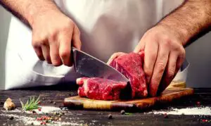 A chef cutting raw beef with a knife