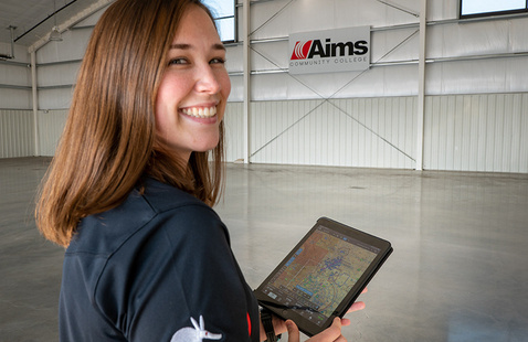 A student in the Aims Aviation Technology Building smiling at the camera while using a tablet