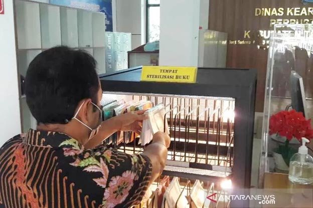 PERPUSTAKAAN. Seorang pengunjung Perpustakaan Umum Daerah Kabupaten Temanggung mengembalikan buku dengan memasukkannya ke boks sterilisasi dalam layanan tanpa sentuh (patuh).