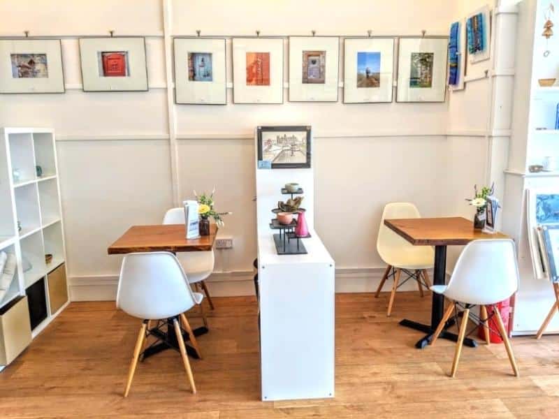 White chairs and wooden tables with art on the walls behind