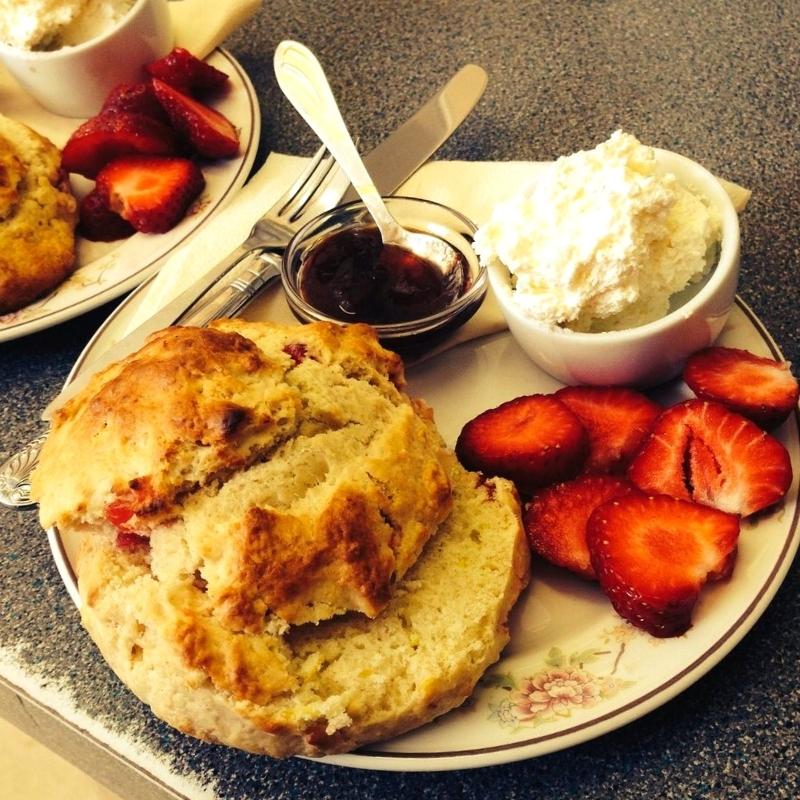 Scone on a plate with fresh strawberries, strawberry jam and clotted cream
