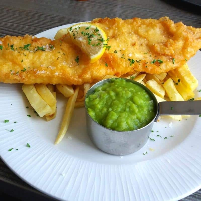 Traditional battered fish, chips and mushy peas on a white plate