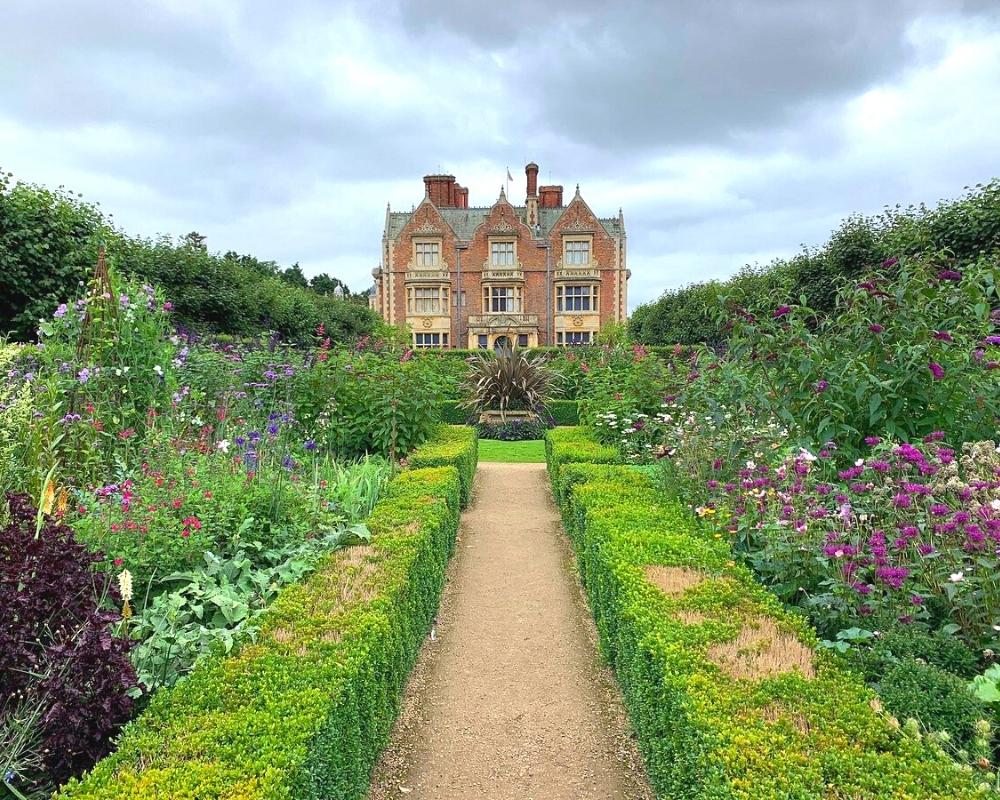 Stately home with herbaceous borders either side of a gravel path