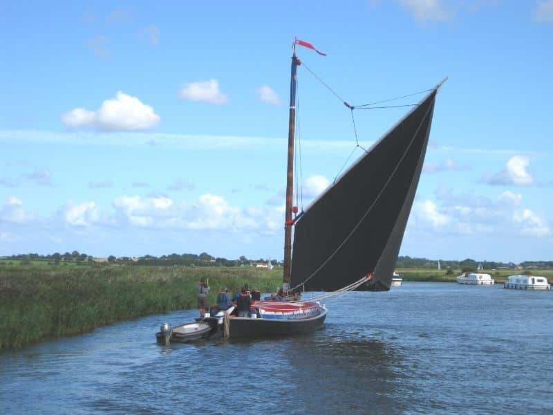 Traditional Norfolk wherry with black sail on a river