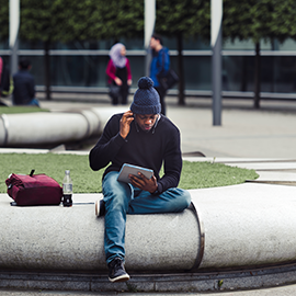 Student sat on Northumbria campus reading book, dressed in blue