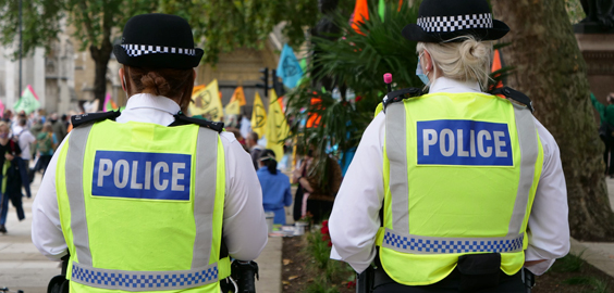 Two police officers wearing police vests. Picture taken from behind them