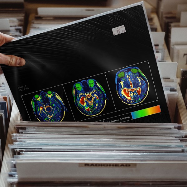 A hand holding a record sleeve with brain scan images in a record store. The sleeve shows three colorful brain scan images against a black background, with a price sticker in the top right corner.