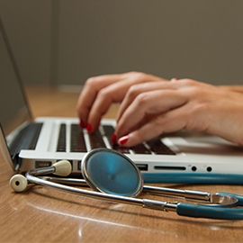 Image of stethoscope with person typing on laptop