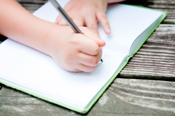 child's hands holding open a journal and writing - one of 75 calming techniques for kids