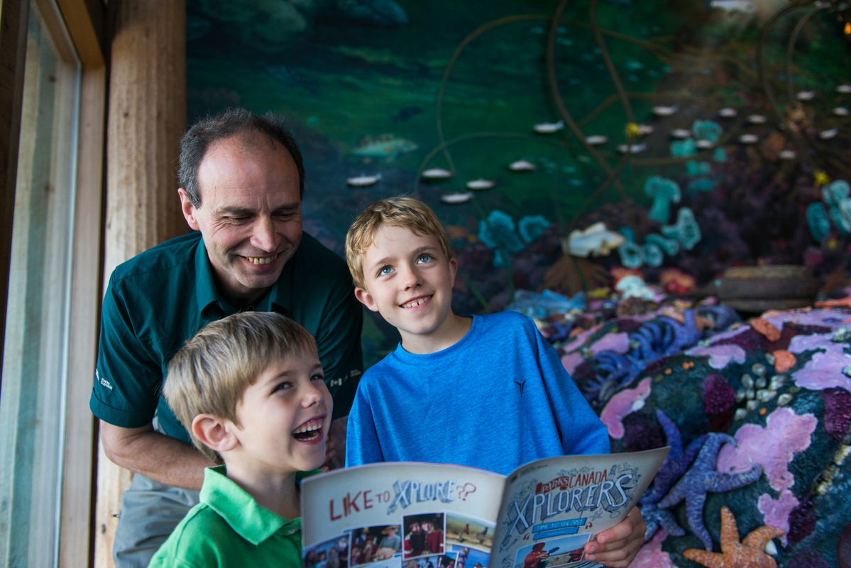 Deux enfants et un employé de Parcs Canada regardant une brochure.