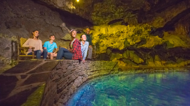 Visitors sit by turquoise thermal waters in a cave