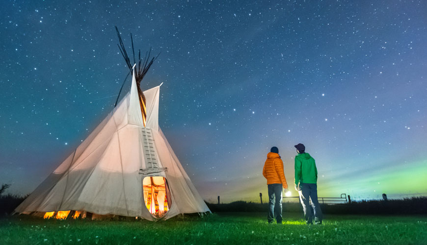 Two visitors gaze at the Big Dipper outside a tipi on a starry night.