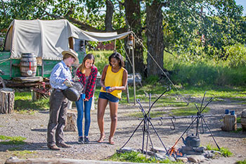 An interpreter pours some cowboy coffee for two visitors at Roundup Camp