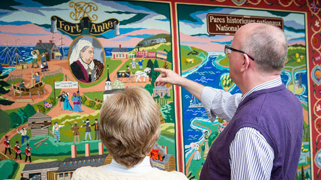 Deux personnes regardent la grande tapisserie accrochée au mur.