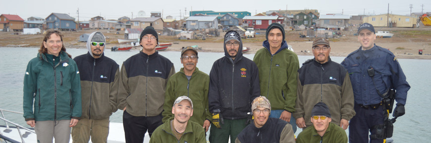  Onze personnes debout sur le rivage, Gjoa Haven est à l'arrière-plan.