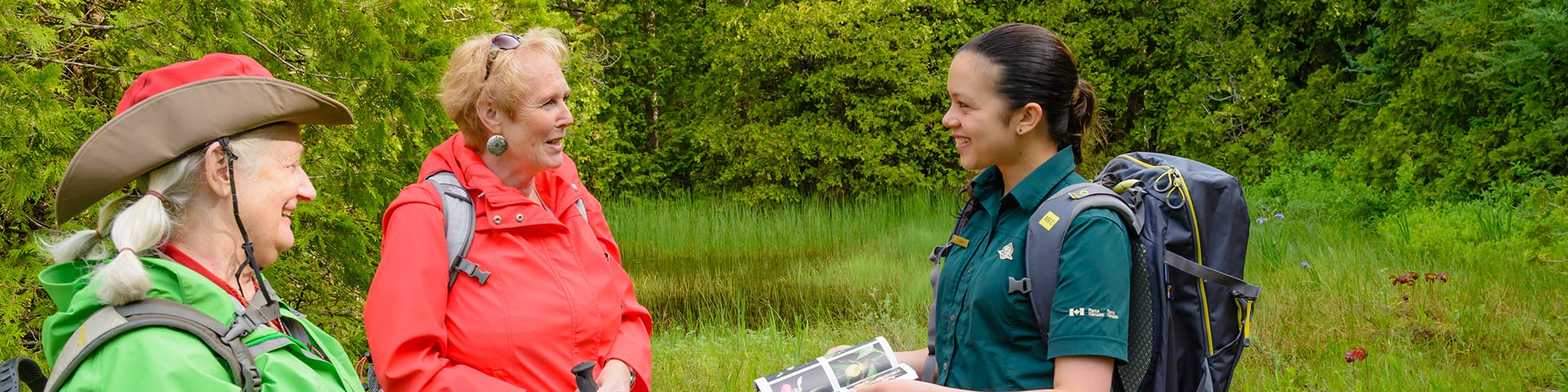 Park staff talks with two hikers in the forest. 