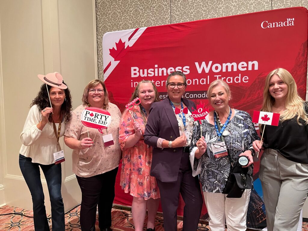 image of 6 women at the Go for the Greens Women's Business conference in Orlando/Disney standing in front of the Canadian Business Women International Trade sign holding Canadian picture party favours