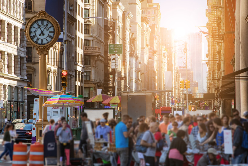 Sunlight shines on the buildings of Manhattan with crowds of people shopping at street vendors in New York City