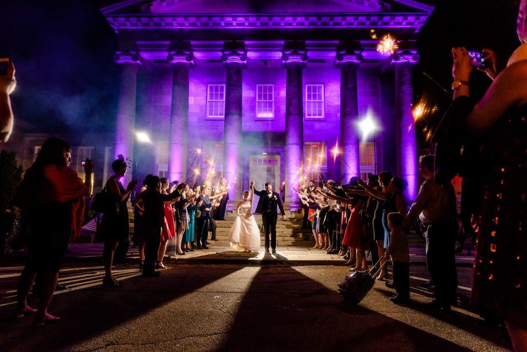 Bride and groom walking out of reception while guests hold sparklers