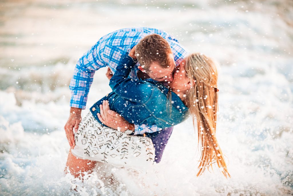 couple having fun in the waves during their beach engagement photoshoot