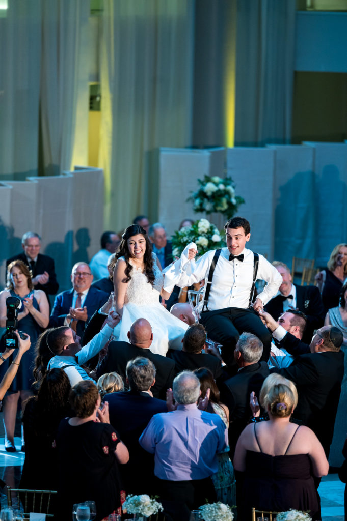 bride and groom in their traditional hora, or chair dance, is the highlight of a Jewish wedding reception. The wedding couple is lifted above the crowd on chairs, while guests sing "Hava Nagila" and circle the couple in a celebratory dance.