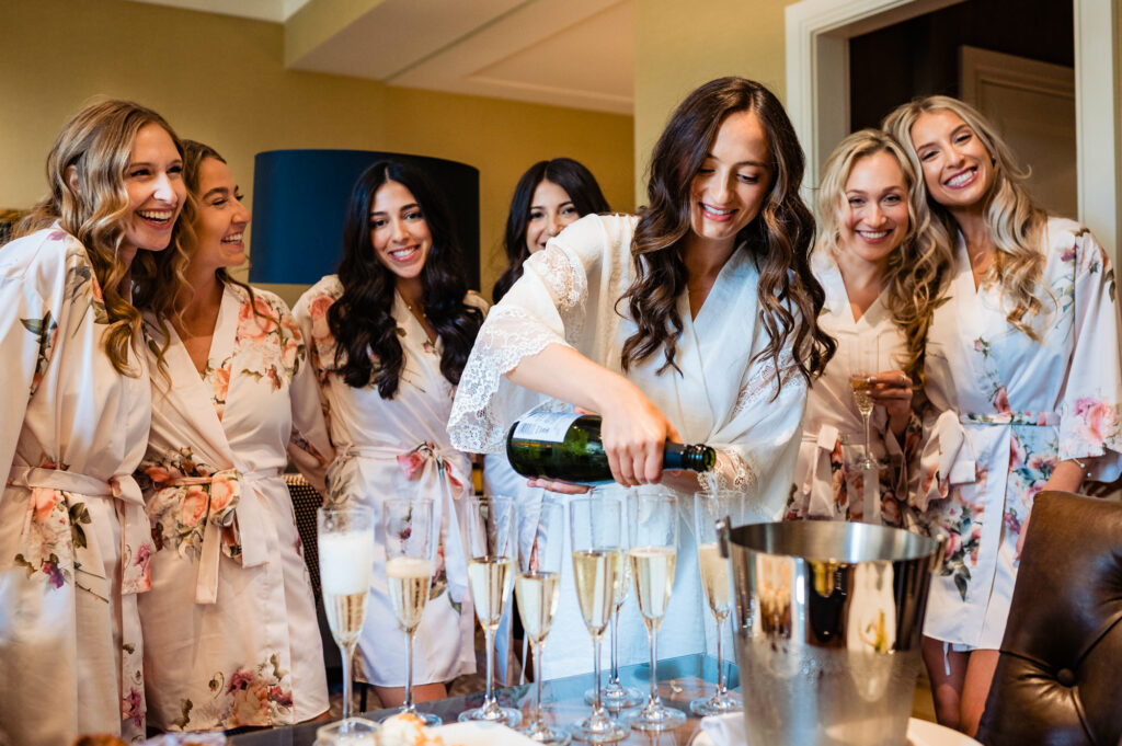 bride pouring champagne on glasses while her bridesmaids watch her