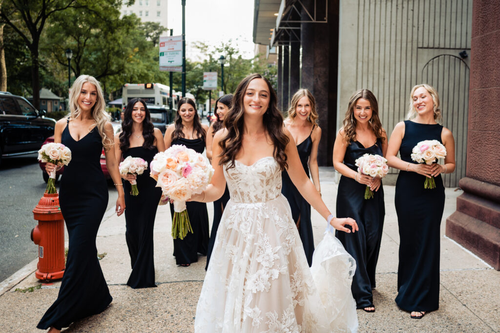 bride taking a pose with her bridesmaids dressed in black gowns on the street