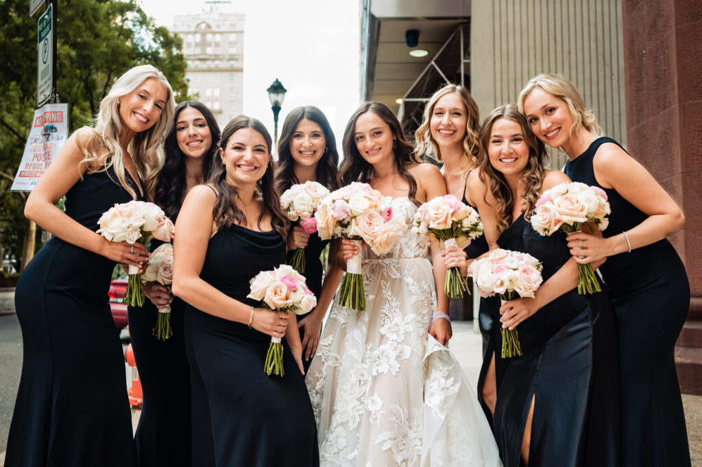 bride taking a pose with her bridesmaids dressed in black gowns on the street
