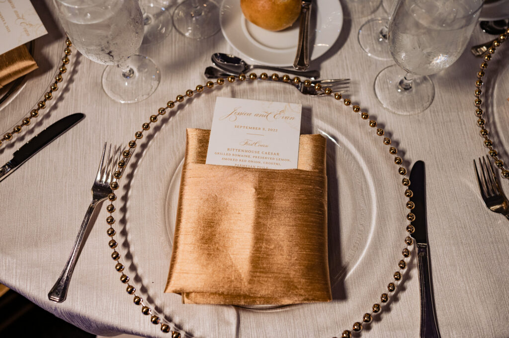 reception menu enclosed in gold colored napkin placed on top of the plate