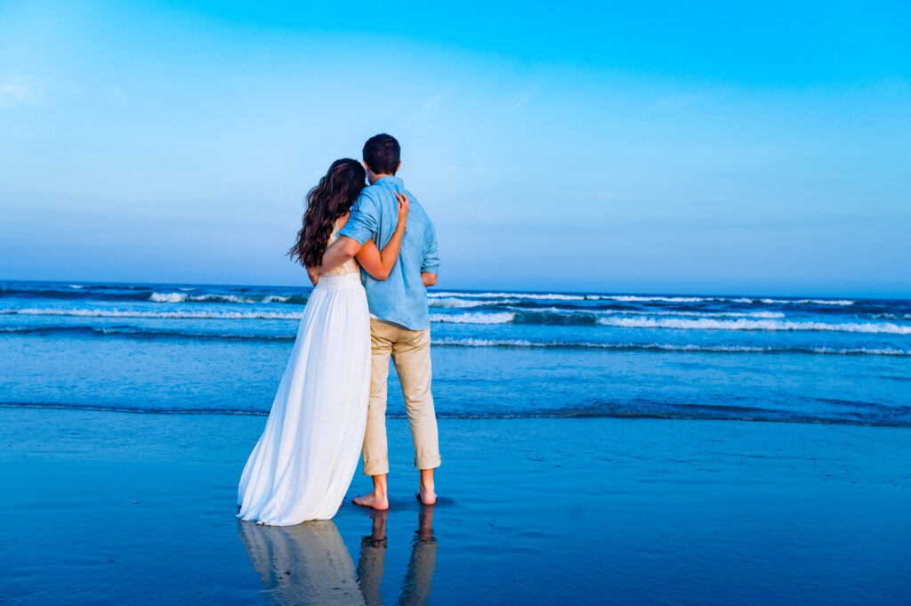 couple stands and hugs on the shores of wildwood New Jersey during their beach engagement session