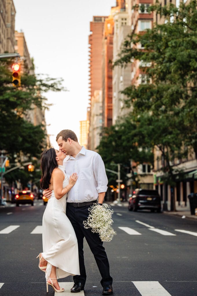 man and woman kissing in the middle of the street while the man holds the flowers in their romantic summer engagement photos