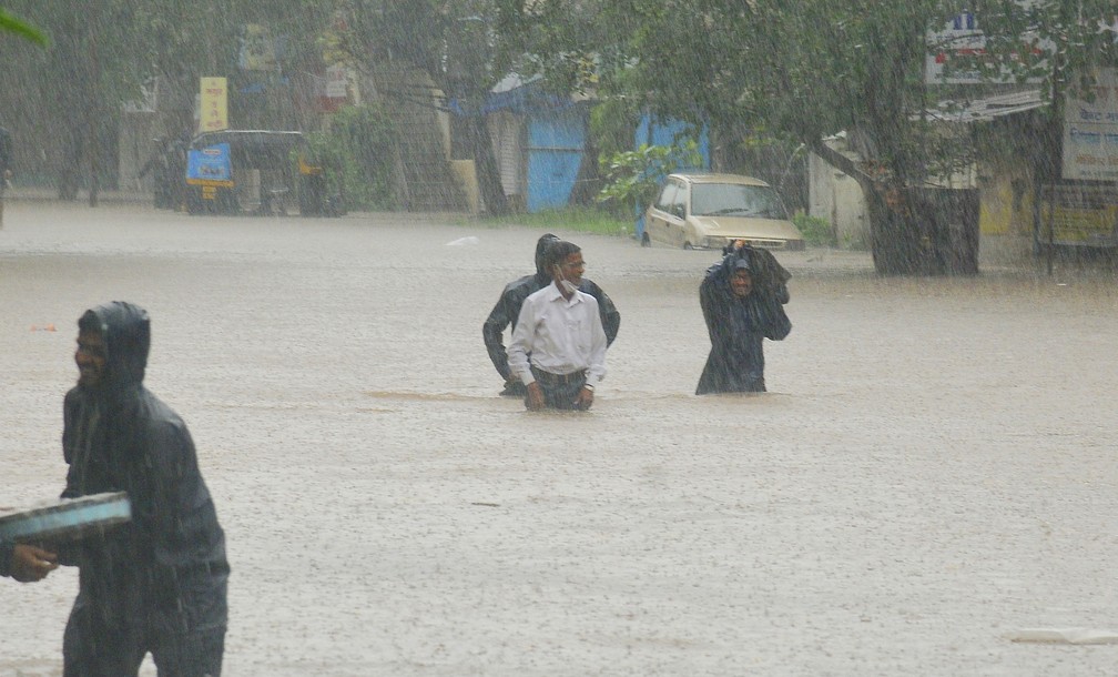 Pessoas atravessam área alagada em Kolhapur, no estado de Maharashtra, em 23 de julho de 2021. Deslizamentos de terra provocados pelas fortes chuvas de monções deixaram dezenas de mortos e desaparecidos no oeste da Índia. — Foto: AP