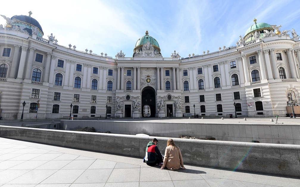 Em Viena, duas pessoas sentam em uma praça vazia. O governo austríaco proibiu reuniões de mais de cinco pessoas  — Foto: Helmut Fohringer/APA/AFP