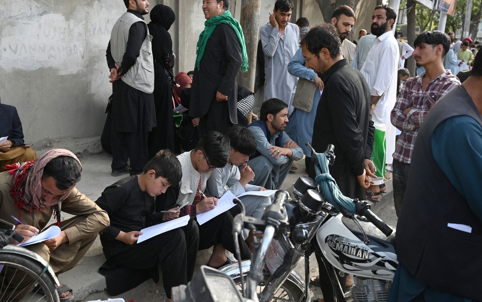  Afegãos preenchem seus dados em requisições para deixar o país em frente às embaixadas do Reino Unido e Canadá, em Cabul, na quinta-feira (19) — Foto: Wakil Kohsar/AFP