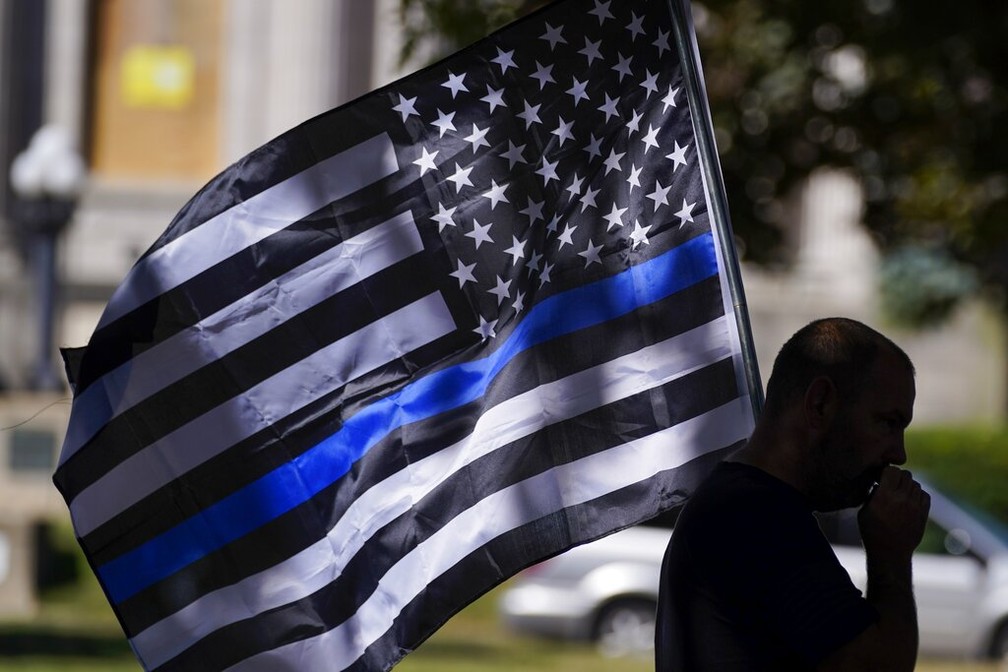 Manifestante usa bandeira dos EUA modificada incluindo faixa azul em homenagem a policiais em Kenosha neste domingo (30) — Foto: Morry Gash/AP Photo
