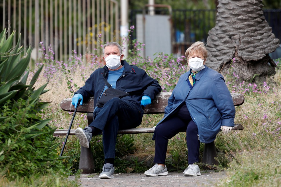 Casal sentado em banco usa máscara durante pandemia do coronavírus em Nápoles, Itália — Foto: Reuters/Ciro De Luca