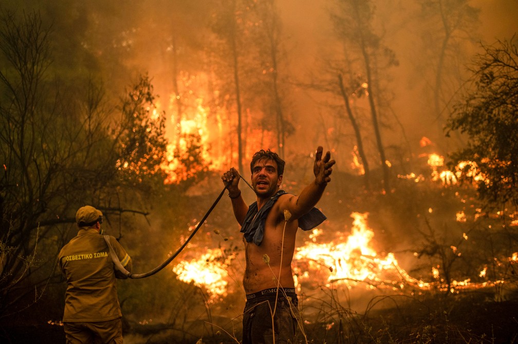 Residente local gesticula enquanto segura mangueira de água vazia em tentativa de extinguir incêndios florestais na Grécia, neste domingo (8) — Foto: Angelos Tzortzinis/AFP