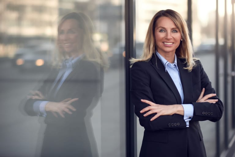 Single confident and attractive female businesswoman in blue suit with grin leaning on window outdoors