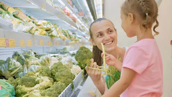 Young mother with little daughter choosing green vegetables in grocery store — together, choice - Stock Photo | #187520550