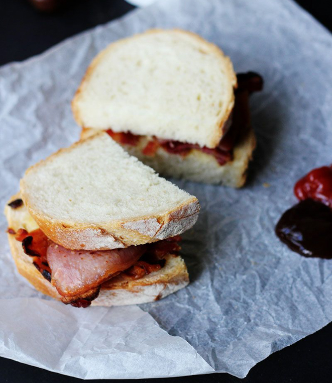 bacon sandwich with ketchup and brown sauce on waxed paper