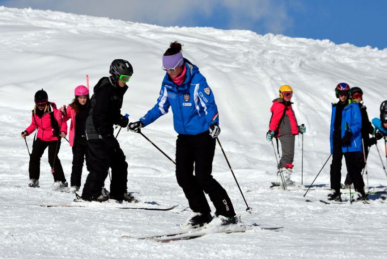 ski instructor in blue jacket leads kids group ski lesson