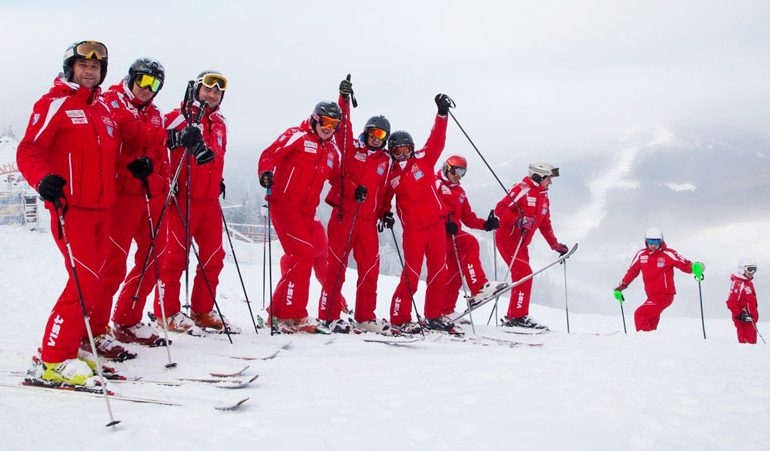 large group of happy ski school instructors in red uniforms