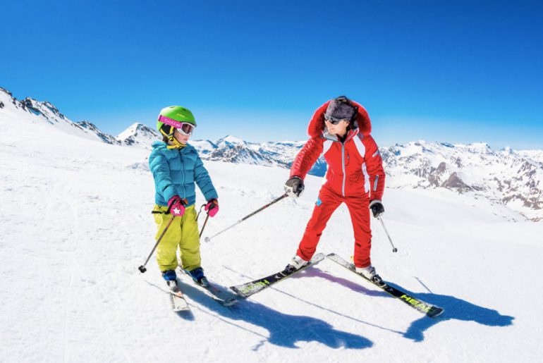 private ski instructor in red ski suit gives tips to child in kids private ski lesson