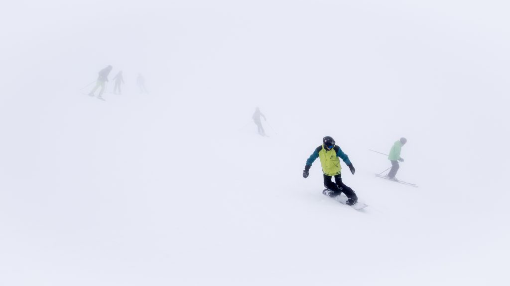 Whiteout: Skiers and snowboarders in thick fog on ski slope in ski resort.