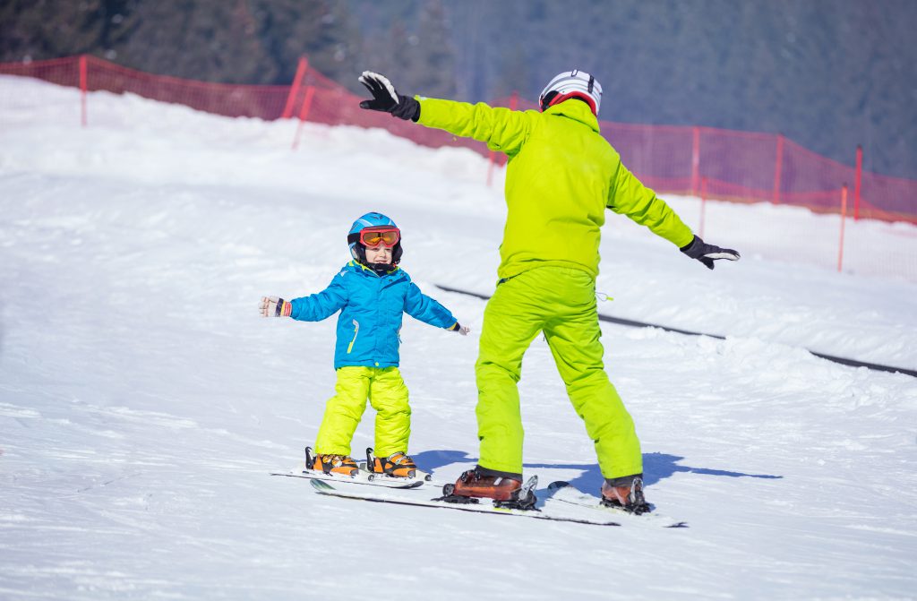 Lesson at skiing school: instructor teaching little skier how to make turns, young boy trying a snow plow turn on slope in children's area