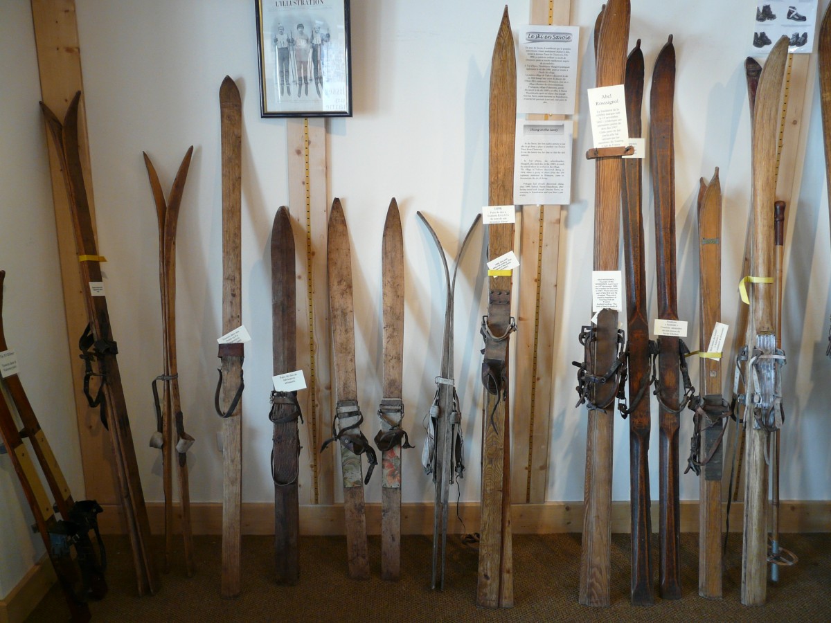 A collection of historical, old wooden skis leaning against a white wall